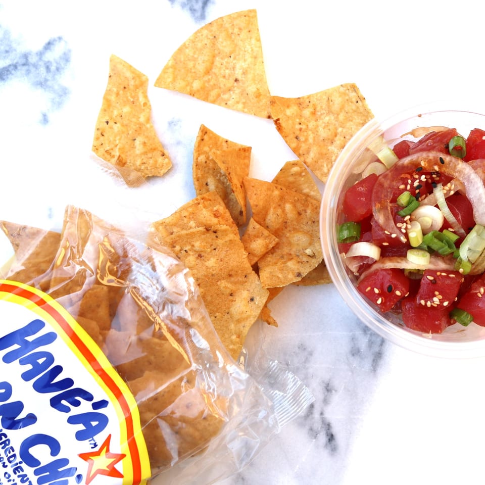 Oh Poke tuna poke bowl with onions and sesame seeds, next to a bag of tortilla chips.
